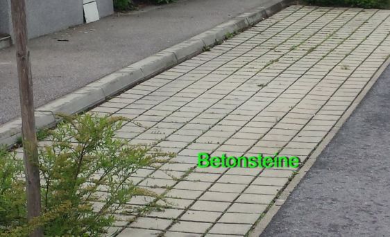 Ein breiter, gepflasterter Weg aus Betonsteinen zwischen Bordstein und Asphalt.